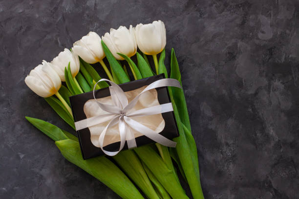 istock White tulip flowers and black gift box on dark background flat lay. Place for text 8 March Happy Womens Mothers Day. 1210493979