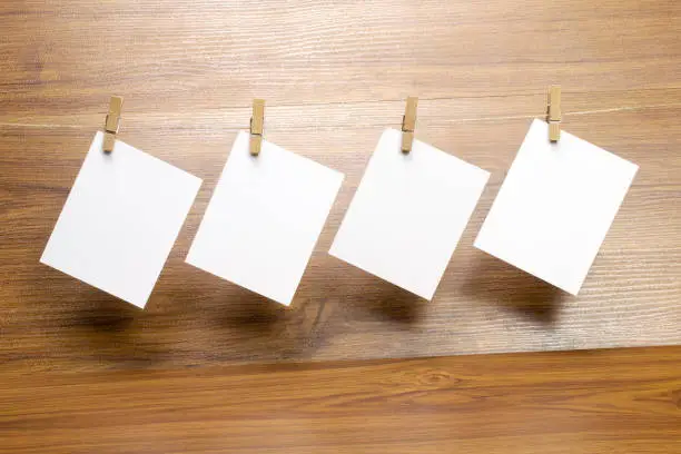 Photo of Empty blank paper frames that hang on a rope with clothespins and isolated on wooden background.