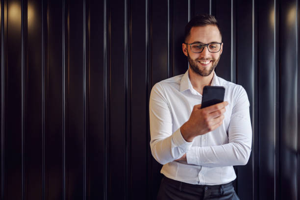 istock Young happy geeky man leaning on the wall and using smart phone for checking on messages on social media. 1210496247