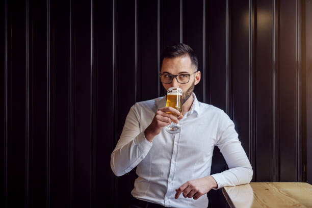 istock Young geeky businessman leaning on the table next to window drinking beer. 1210496701