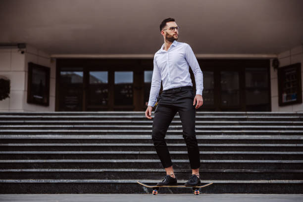 istock Full length of attractive unshaven man elegantly dressed riding skateboard. 1210498754