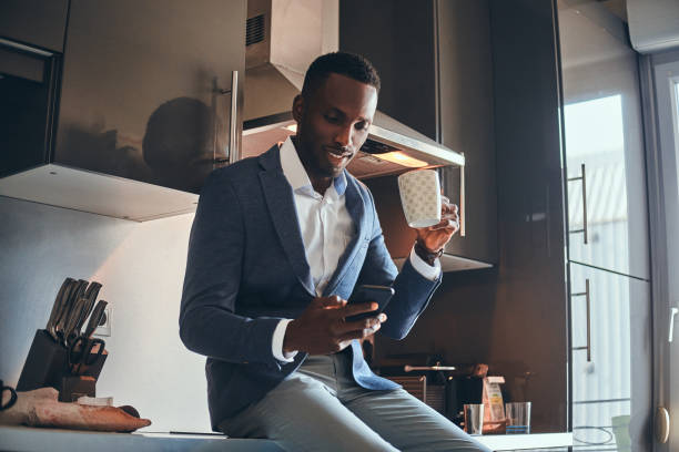 Concept of mourning routine - man has coffee at the kitchen Happy smiling businessman is enjoying his morning coffee while chatting by mobile phone at his kitchen. well dressed stock pictures, royalty-free photos & images