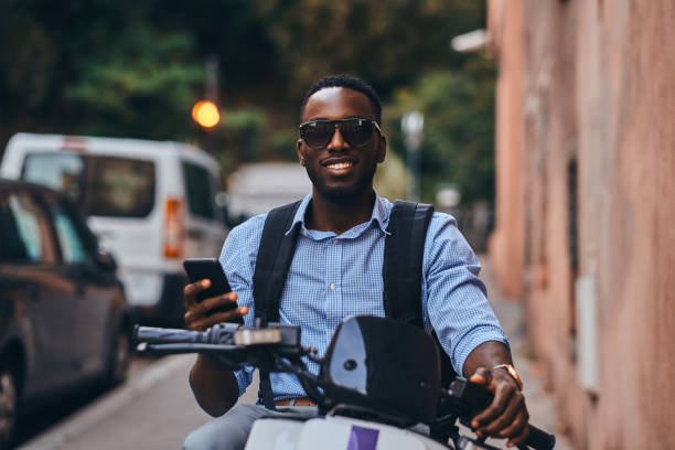 istock Young black man on scooter with mobile phone 1210508094