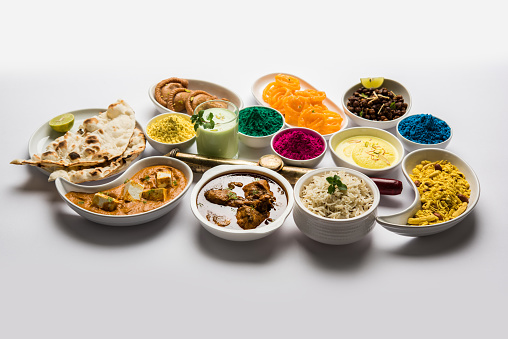 Happy Holy concept  showing Indian assorted lunch food like paneer butter masala, naan, jeera rice, black chana fry, jalebi, fujiyama, thandai and Farsan with holi colours and pichkari