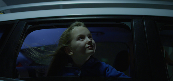 Medium shot of girl leaning out car window at night