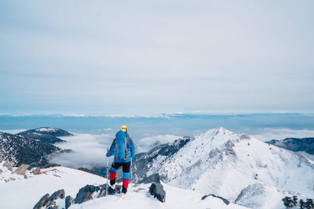 elderly alpine mountain climber is looking at the scenery in the summit of a high altitude mountain in winter - weather time travel locations nature imagens e fotografias de stock