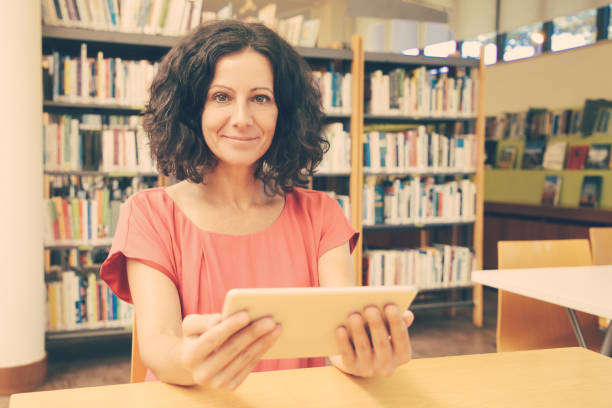 istock Satisfied female customer with gadget posing in public library 1210518704