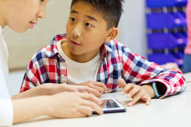 istock Schoolboy looking at friend holding digital tablet 1210519279