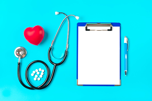 Phonendoscope, heart, tablet with white paper, pen, medicine on blue background Health, life, Medical Insurance concept Top view Flat lay Mock up.