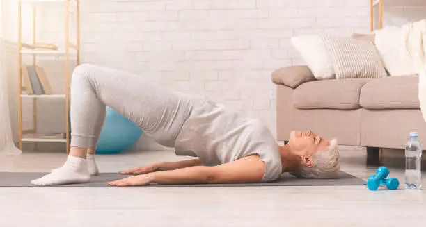Active senior woman doing back exercise on floor at home, panorama