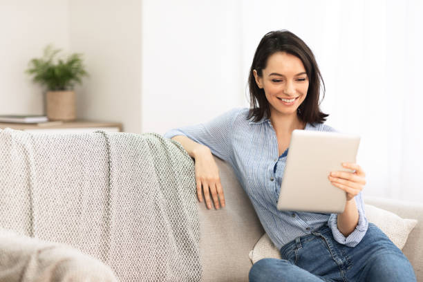istock Young woman using digital tablet sitting on couch 1210523573