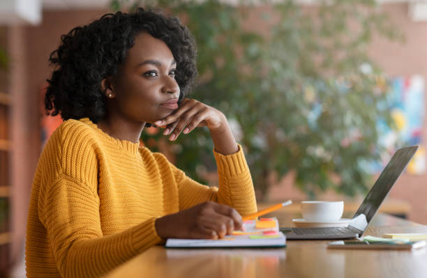 Thoughtful afro woman looking for new job online Thoughtful afro young woman looking for new job online, using laptop at cafe, taking notes, side view, copy space mindfulness photos stock pictures, royalty-free photos & images