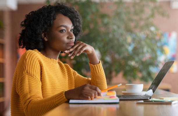 Thoughtful afro woman looking for new job online Thoughtful afro young woman looking for new job online, using laptop at cafe, taking notes, side view, copy space bushy stock pictures, royalty-free photos & images