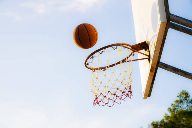 istock Old grunge basketball falling into old grunge basket and backboard on blurred sky background 1210523697