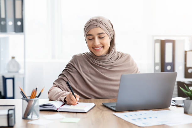 istock Islamic businesswoman working on laptop in office and writing notes 1210523733