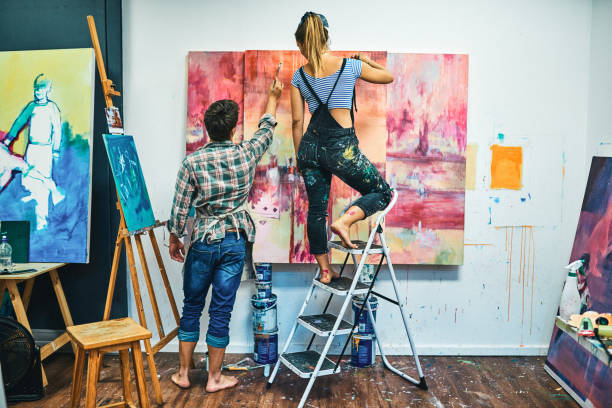 Help me, babe Full length shot of an unrecognizable couple standing together and painting on a canvas in their art studio workshop art studio art paint stock pictures, royalty-free photos & images
