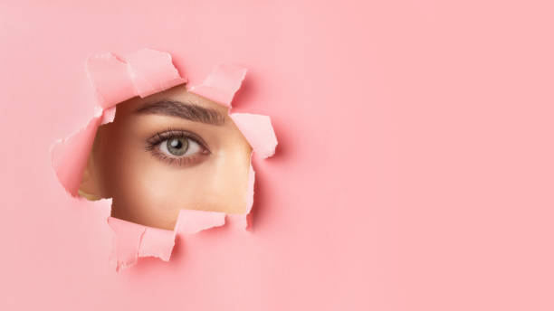 istock Unrecognizable Girl Looking At Camera Through Hole In Pink Paper 1210523910