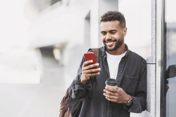 joven alegre usando teléfono inteligente en una ciudad - mensaje de texto fotos fotografías e imágenes de stock