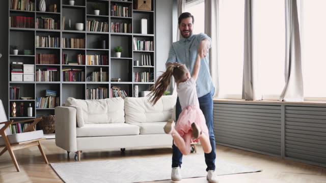 Loving father having fun spinning with child daughter at home