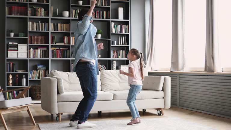 Active cheerful dad dancing having fun with kid at home