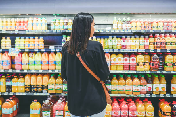 Juices in all the colours of the rainbow Rearview shot of a young woman shopping in a grocery store refrigerated section supermarket photos stock pictures, royalty-free photos & images