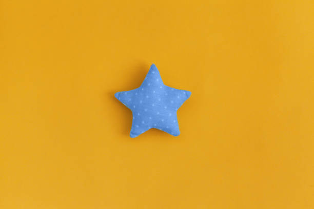 Soft blue pillow in shape of star. Blue pillow on yellow background. stock photo