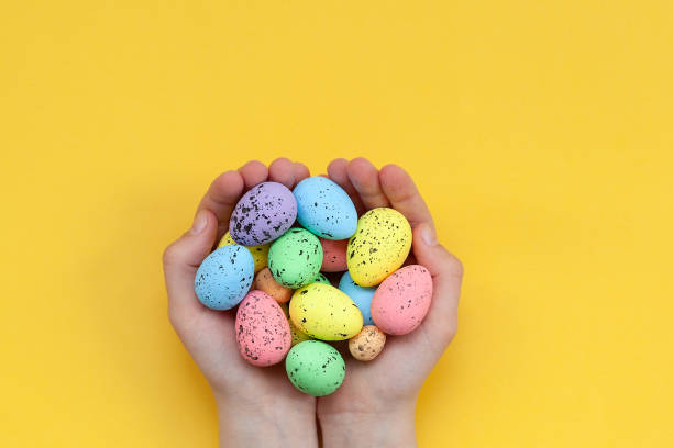 istock Kid's hands holding colorful painted easter eggs on yellow background. Easter concept. 1210534577
