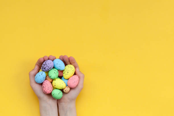 istock Kid's hands holding colorful painted easter eggs on yellow background. Easter concept. 1210534704