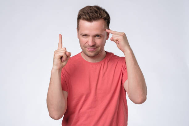 Satisfied young man showing index fingers up, generating idea. Studio shot