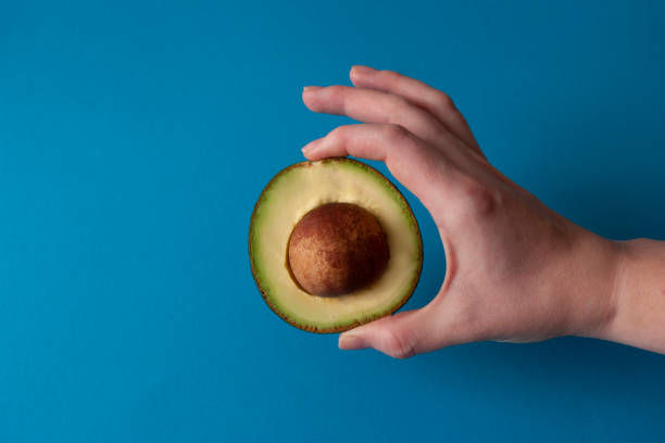istock Half of avocado holding hand on blue background 1210534904