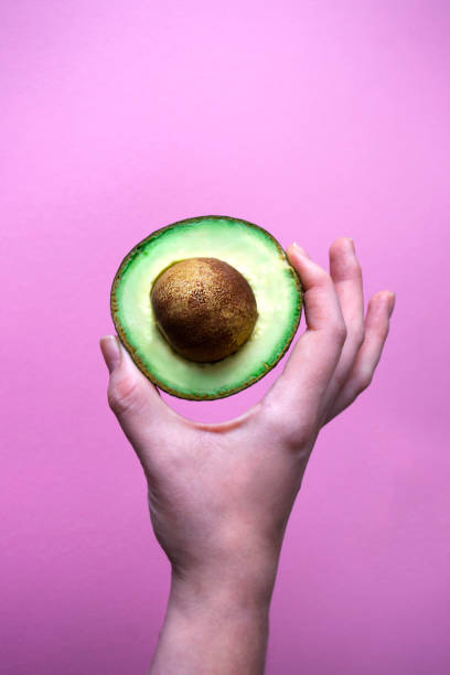 istock Hand holding half of avocado fruit on pink background. 1210534942