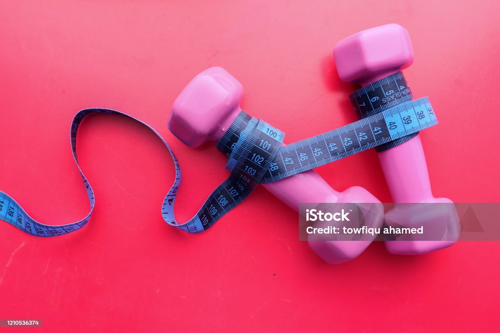 top view of dumbbell and measurement tape on pink background top view of dumbbell and measurement tape on pink background. Dieting Stock Photo