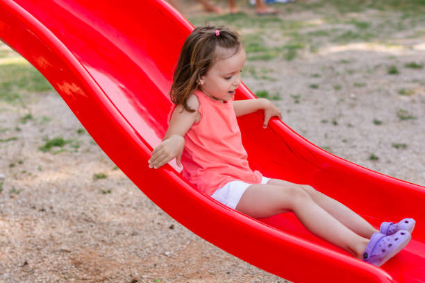 A young girl enjoys playful moments on a bright blue playground slide at a neighborhood park. Autumn leaves and warm light create a cheerful, carefree day.