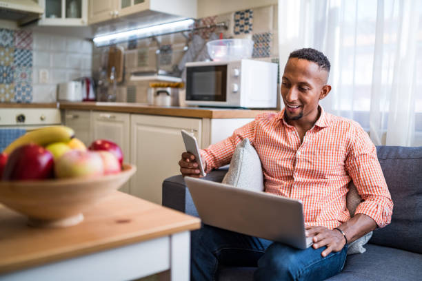 Afro latino men working on a laptop and using smart phone at home Afro latino men working on a laptop at home afro latinx ethnicity stock pictures, royalty-free photos & images