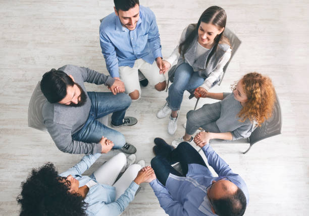 istock Group therapy patients sitting in circle and holding hands during session 1210545315