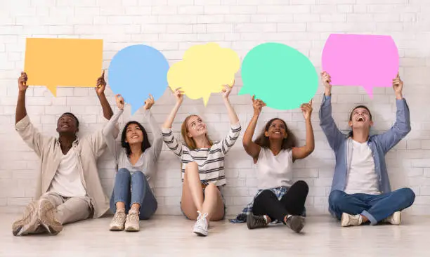 Photo of Group of teenagers sitting on floor, holding speech bubbles above