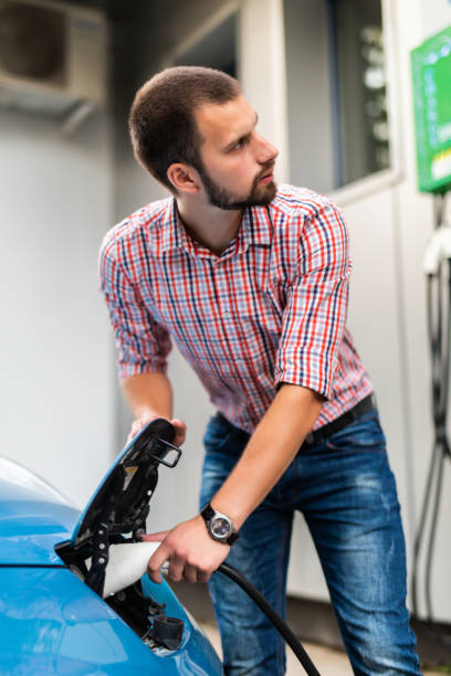 istock Young handsome Man plugging cable to electric car at station 1210547015