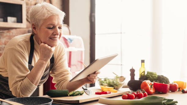 istock Cheerful senior woman using digital tablet at kitchen, reading news 1210547863