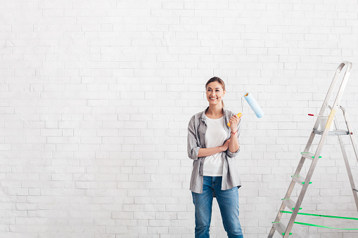 Thoughtful woman holding paint roller, thinks about refurbishment of walls in new house. Repair, building, home concept, copy space