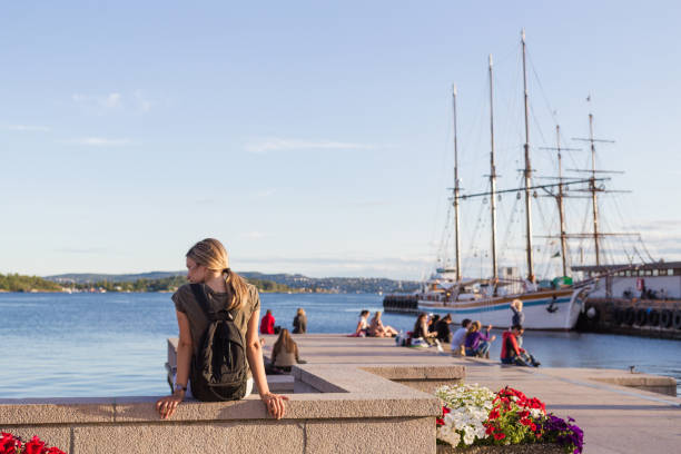Modern carefree female tourist visiting Oslo, sitting on a dock and enjoying the view