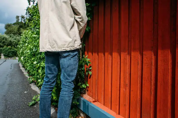 Young rude man peeing on a wooden fence