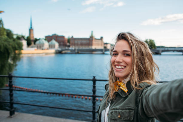 Modern fashionable woman taking photo of hersefl in front of Gamla Stan Modern young woman on rainy day taking selfie in front of colorful Gamla Stan in Sweden swedish woman stock pictures, royalty-free photos & images