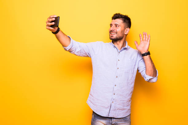 istock Smiling young man make selfie by mobile phone standing isolated over yellow background. 1210551589