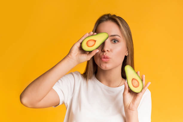 istock Cheerful Girl Posing With Avocado Halves On Yellow Background In Studio 1210551667