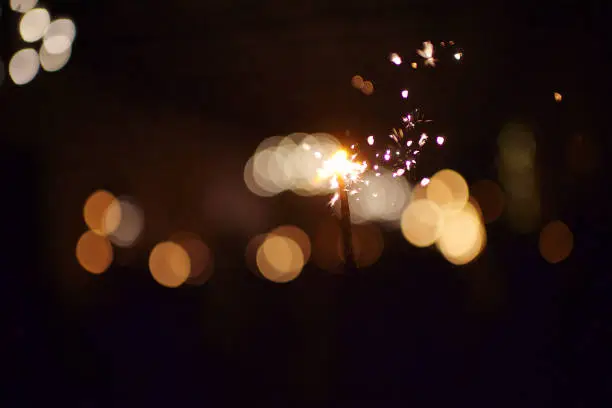 Selective focus Sparkling Sparkler with sparks flying with string light backdrop defocussed at night