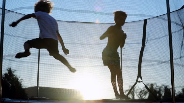 Silhouette of children bouncing inside trampoline outside in the sunset