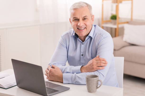 istock Senior man using laptop at office and looking at camera 1210553566