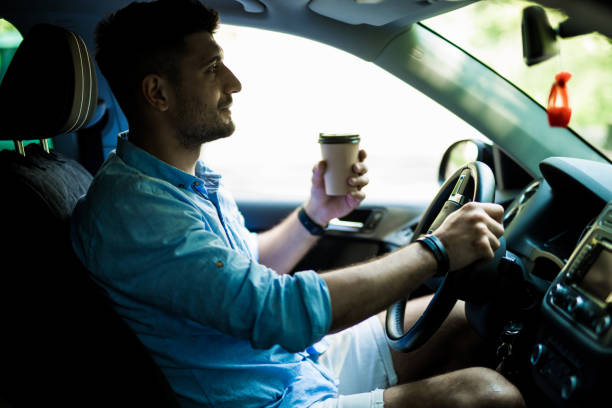 istock Transportation and vehicle concept. Young man drinking coffee while driving the car 1210556404