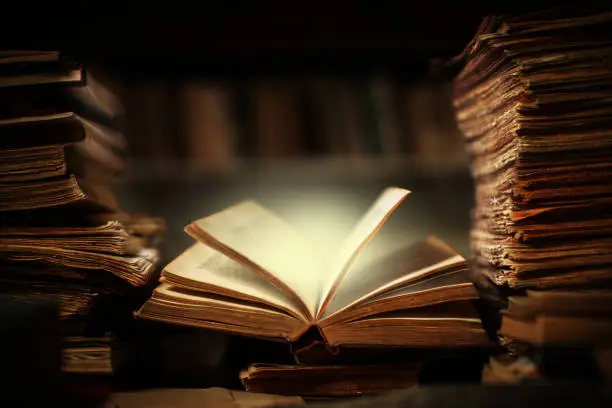 Magical book lying open on desk in library. Glowing pages illuminates surrounding.