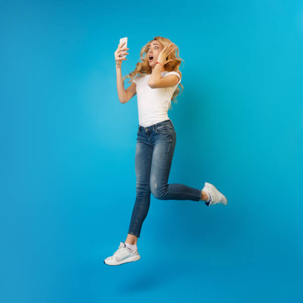 istock Wow! Shocked woman jumping and using phone 1210558879